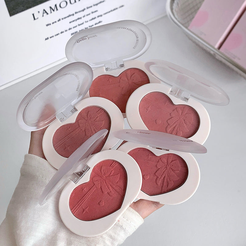 Heart-shaped blushes in a compact case held by a hand.