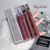 Four lip glosses with a box labeled 'Gege Bear' on a textured surface.
