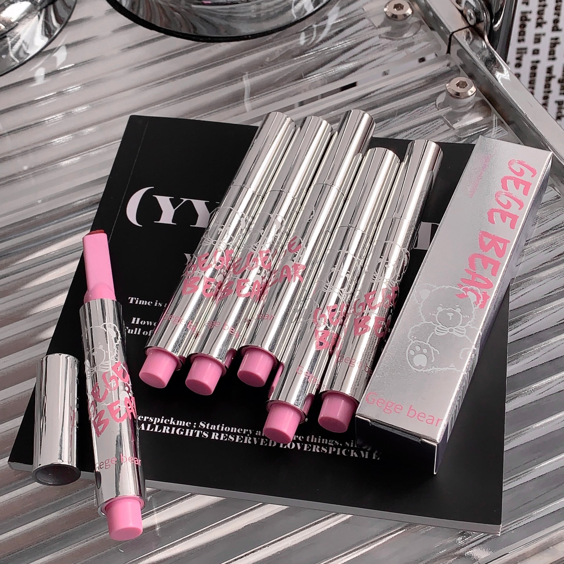 Set of silver and pink lip products with a box on a reflective surface