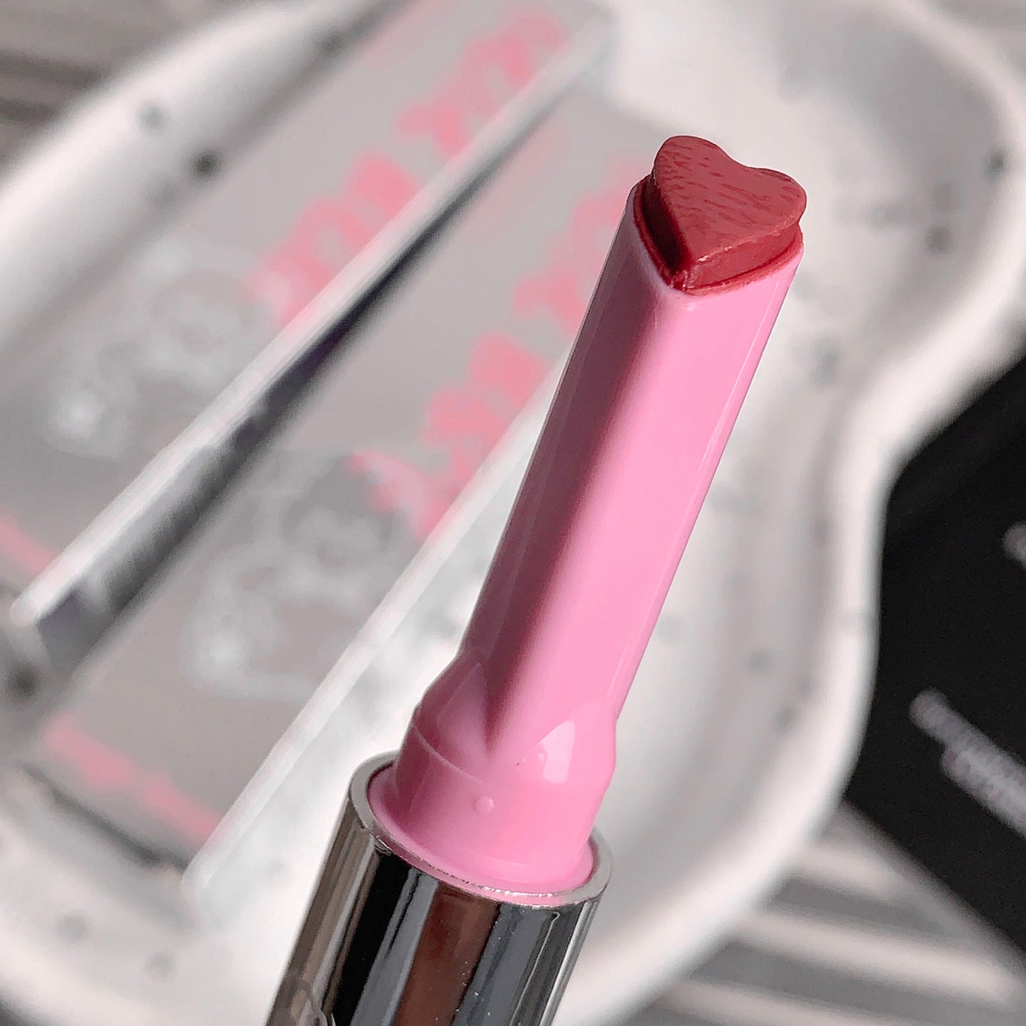 Pink lip gloss with heart-shaped cap on a blurred background