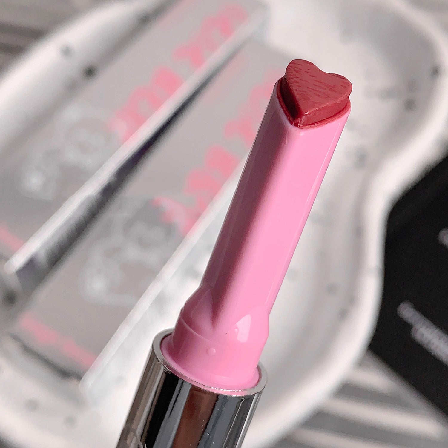 Pink lip gloss with heart-shaped cap on a blurred background