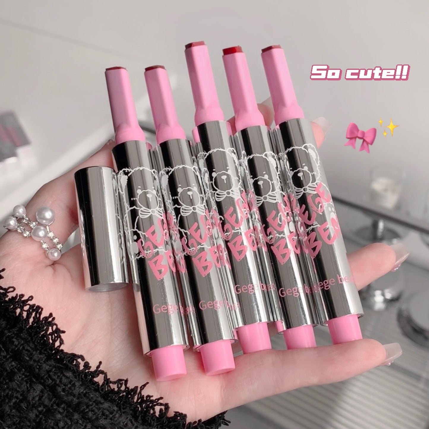 Set of pink and silver lip glosses held in a hand with decorative text on the packaging.