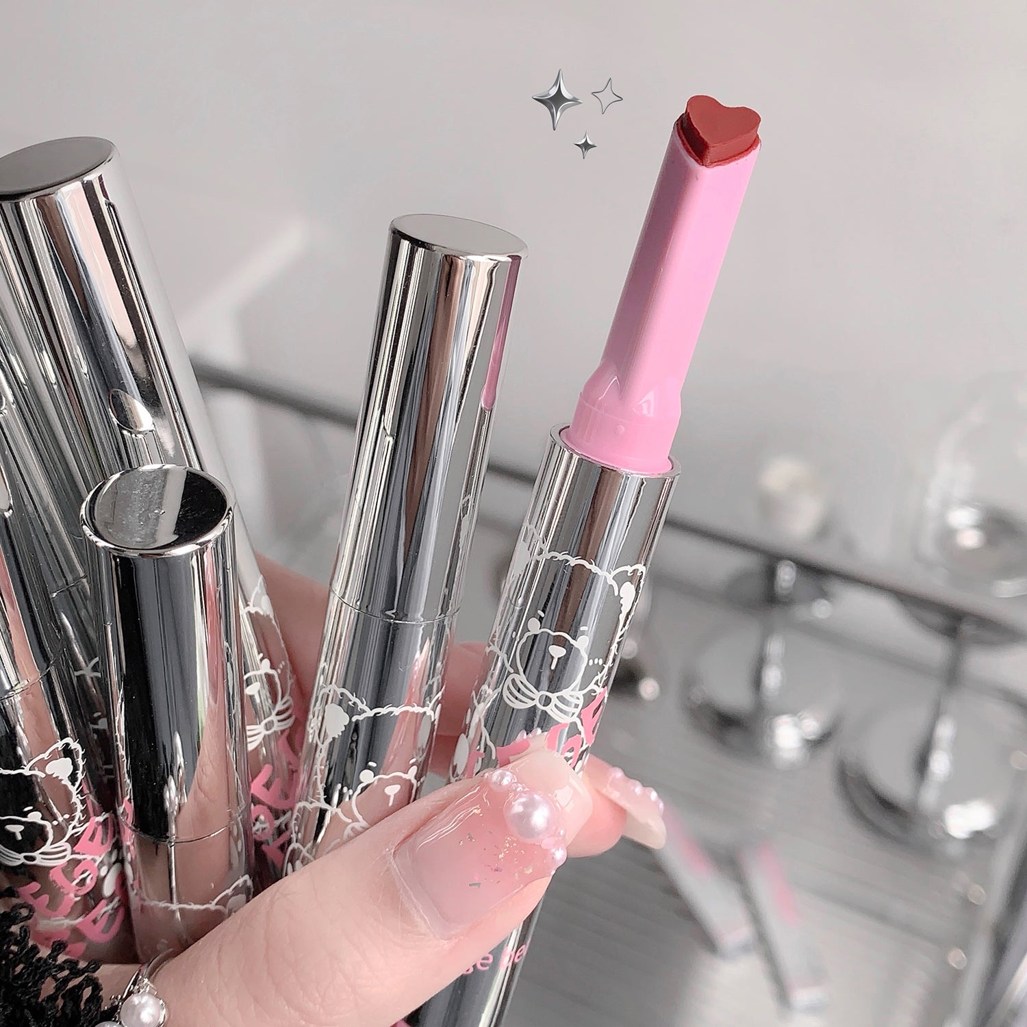 Hand holding a pink and silver lipstick with a starry background