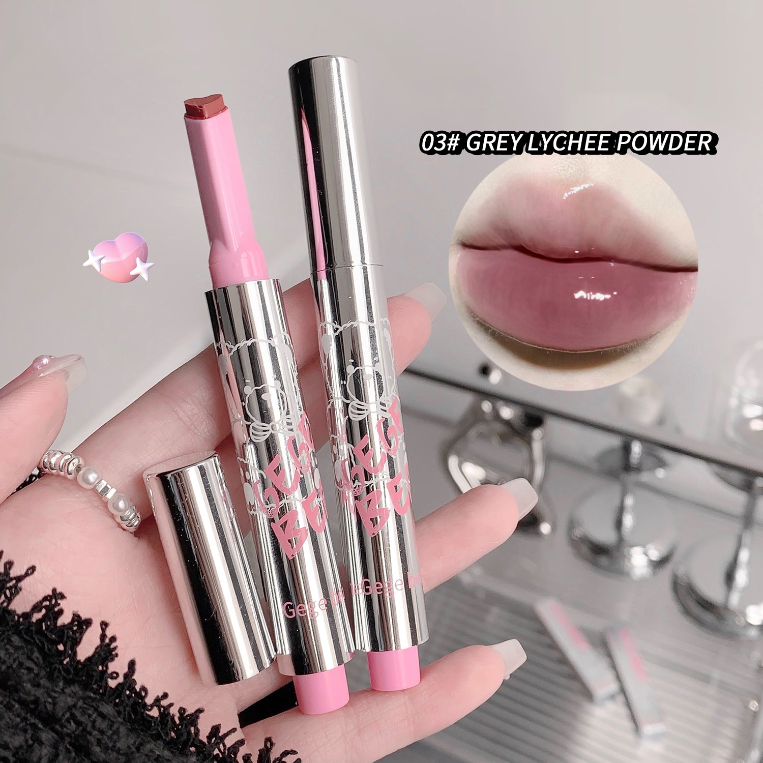 Two lipsticks with pink caps and silver bodies, one being held by a hand, on a neutral background.