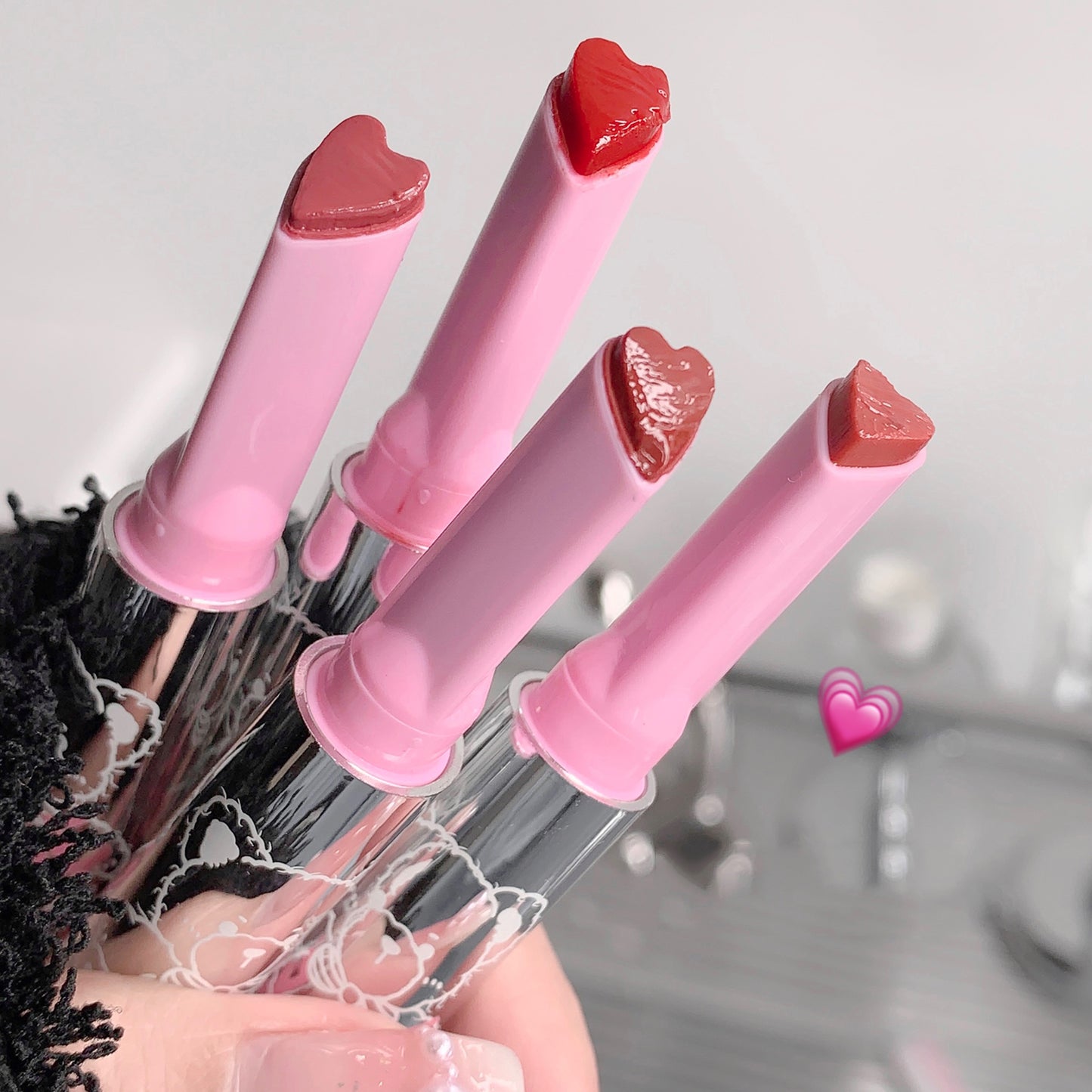 Set of pink hair curlers with heart-shaped ends held by a person.