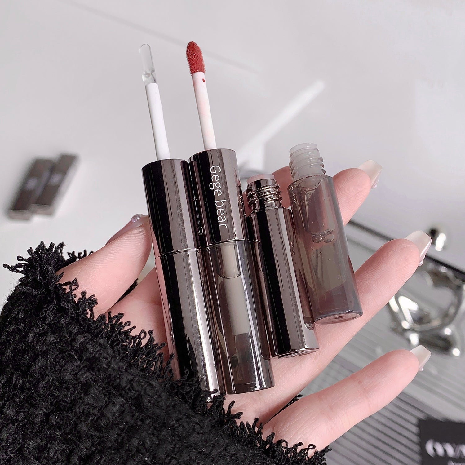 Hand holding makeup products including lipsticks and a lip liner on a blurred background