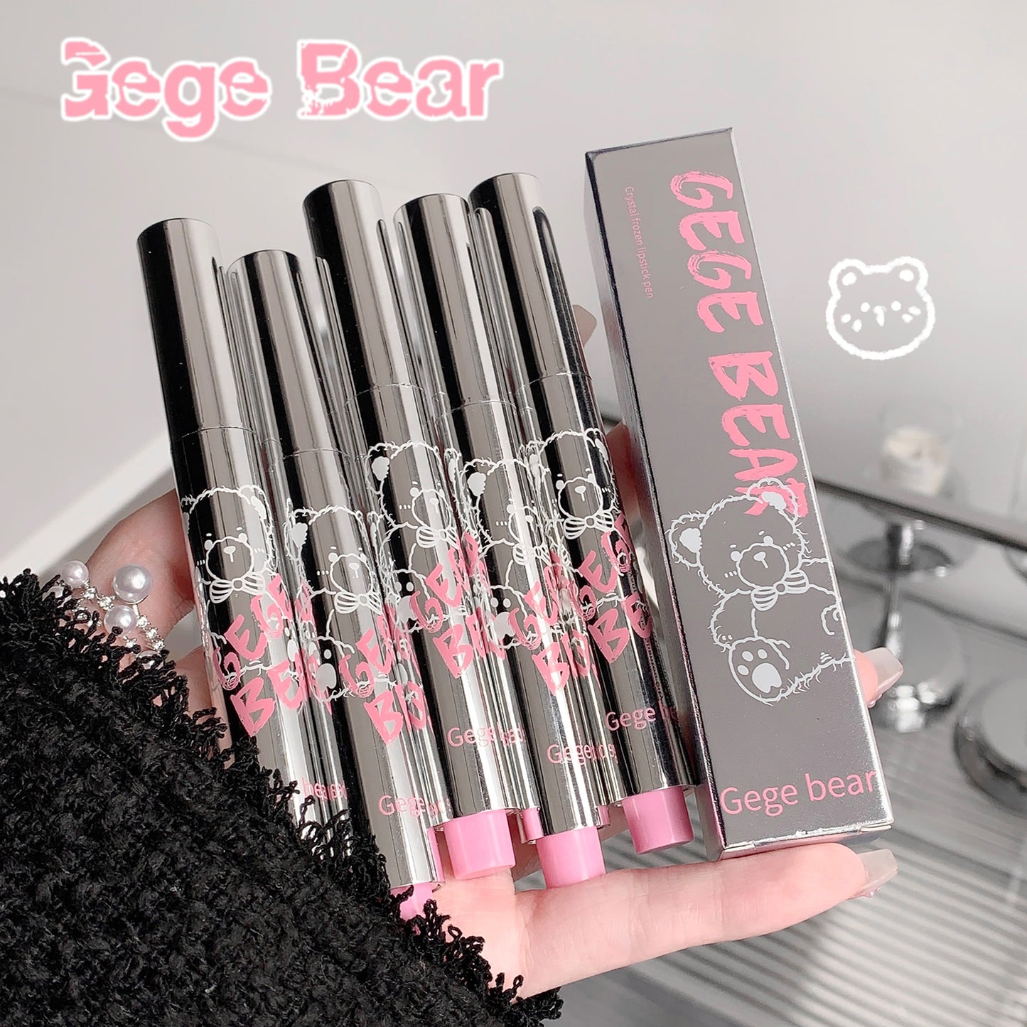 Four silver lip glosses with pink accents and 'Gege Bear' branding held by a hand.