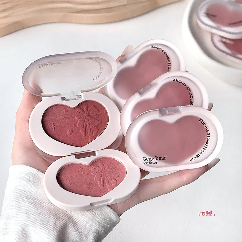 Heart-shaped blush compact with pink blush color held in a hand on a white background