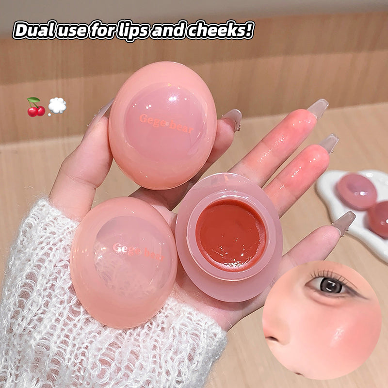Pink lip balm with dual use for lips and cheeks, held by a hand.