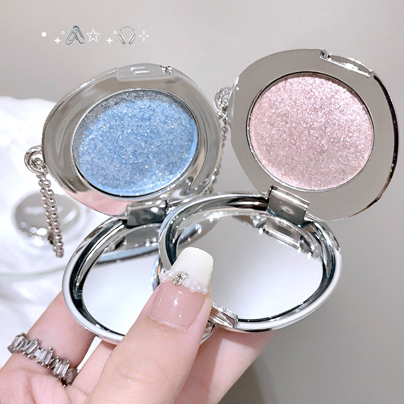 Two compact mirrors with glittery contents held by a hand against a neutral background