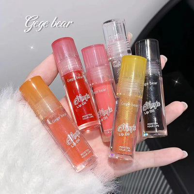 Collection of 'Magic Lip Oil' lip balm tubes held in a hand against a light background.