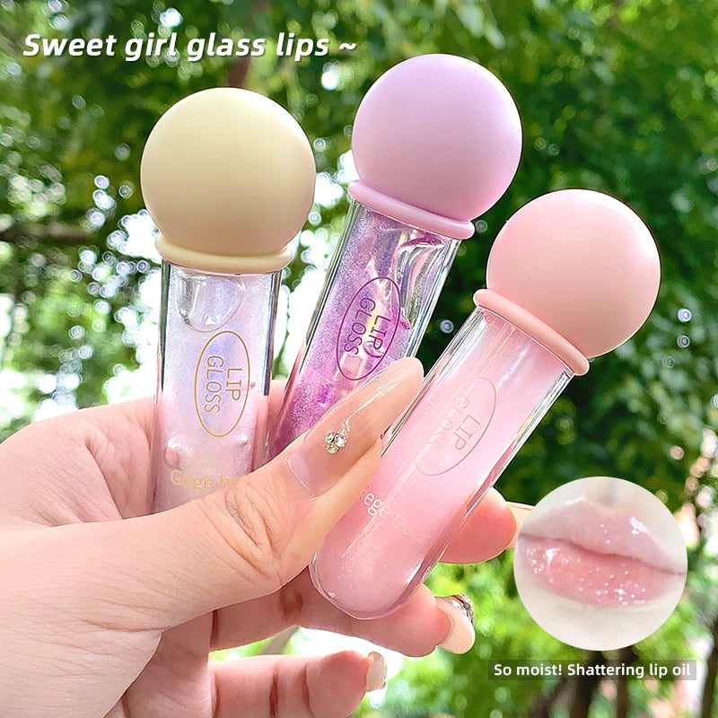 Three lip glosses in different colors held by a hand with a green leafy background.