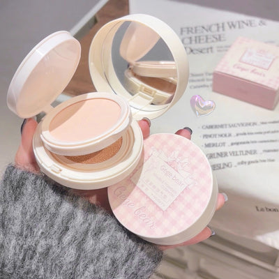 Compact powder with a mirror held by a hand, with a magazine in the background.