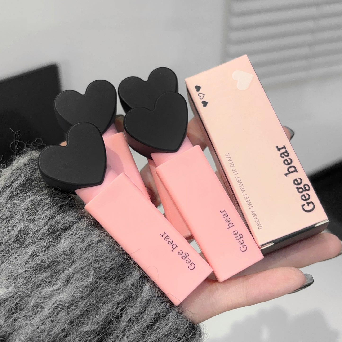 Pink lip balm with black heart-shaped ends held by a person, with 'Gegebear' packaging.