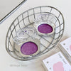 Three purple bear-shaped containers in a wire basket on a light surface.