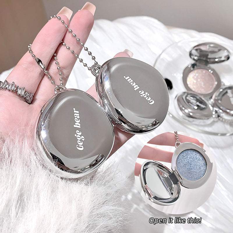Silver compact mirror with 'Gege bear' branding held by a hand, with a blurred background of similar mirrors.