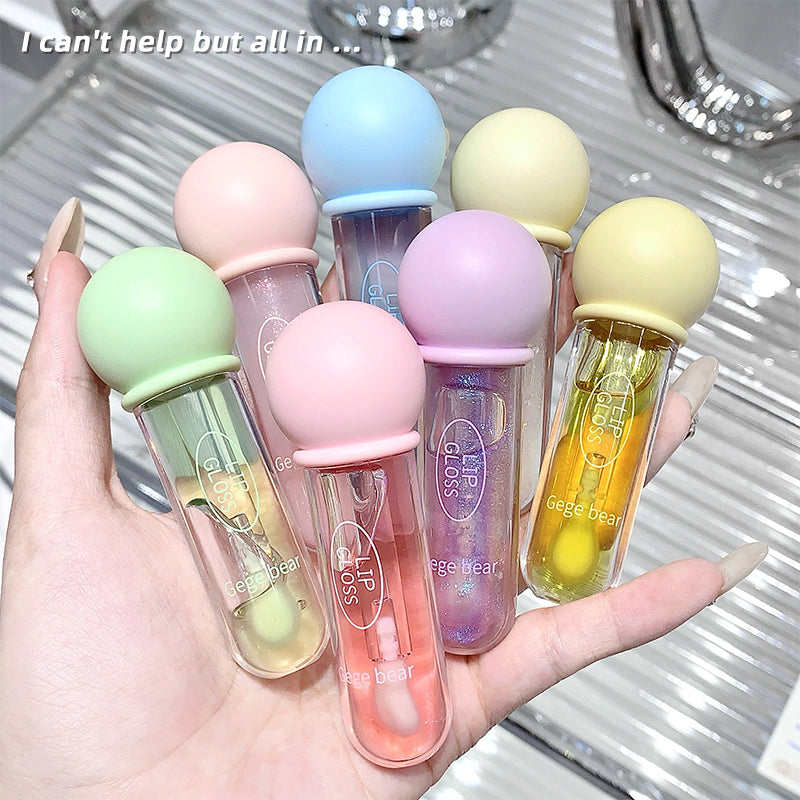 Hand holding six small lip gloss bottles with colorful caps on a reflective surface.