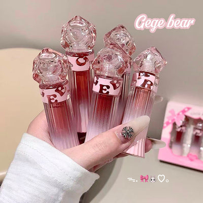 Set of pink lip glosses with geometric designs held by a hand, branded 'Gege bear'.