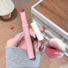 Hand holding a pink lip pen and white lip balm with a blurred background