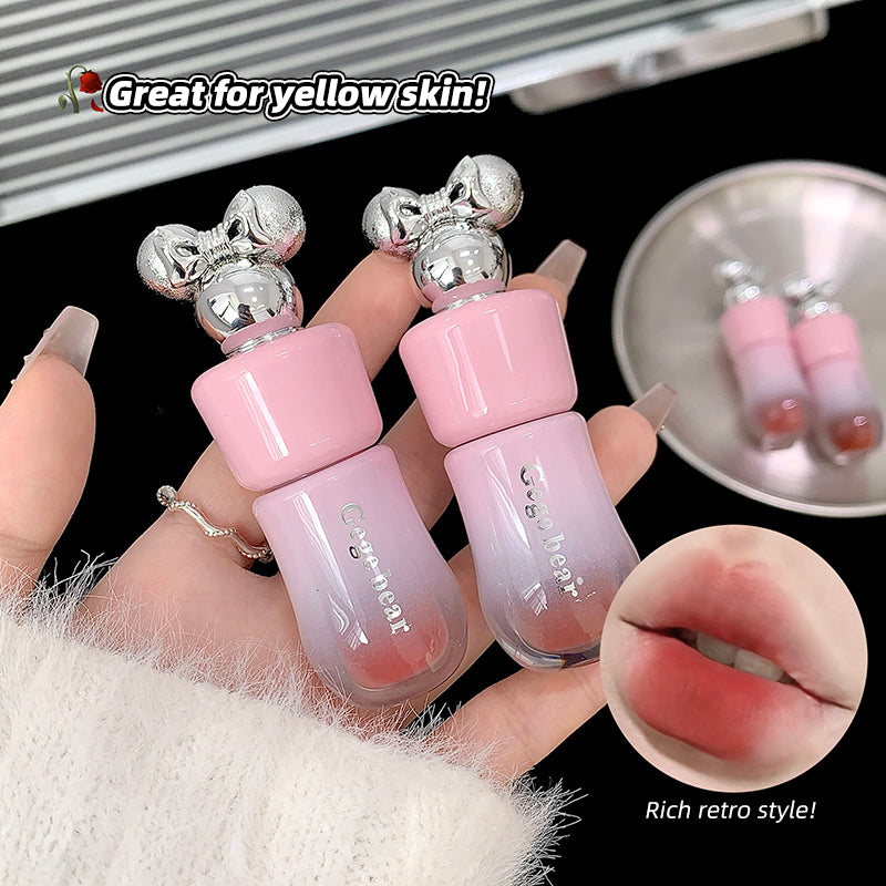 Two pink lip glosses with silver tops held by a hand, with a close-up of lips wearing the product and text indicating it's great for yellow skin.