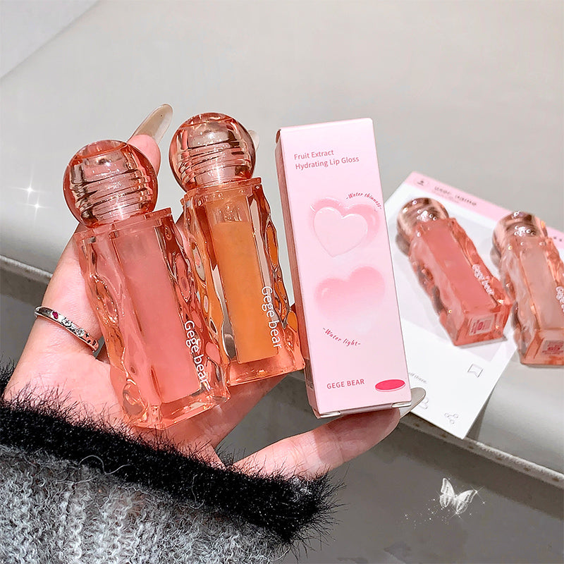 Two lip glosses and their packaging held in a hand with a blurred background