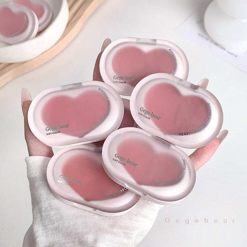 Heart-shaped pink items with 'Gegebear' branding held by a hand on a light background.