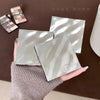 Two silver compact mirrors with a brand logo held by a hand on a brown surface.