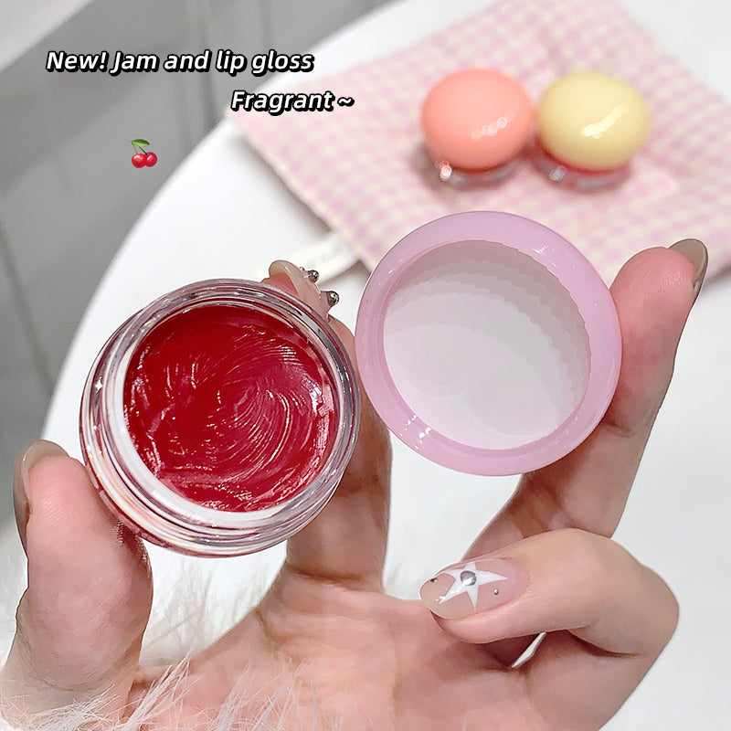 Hand holding a small container of red jam with a pink lid, on a white background.
