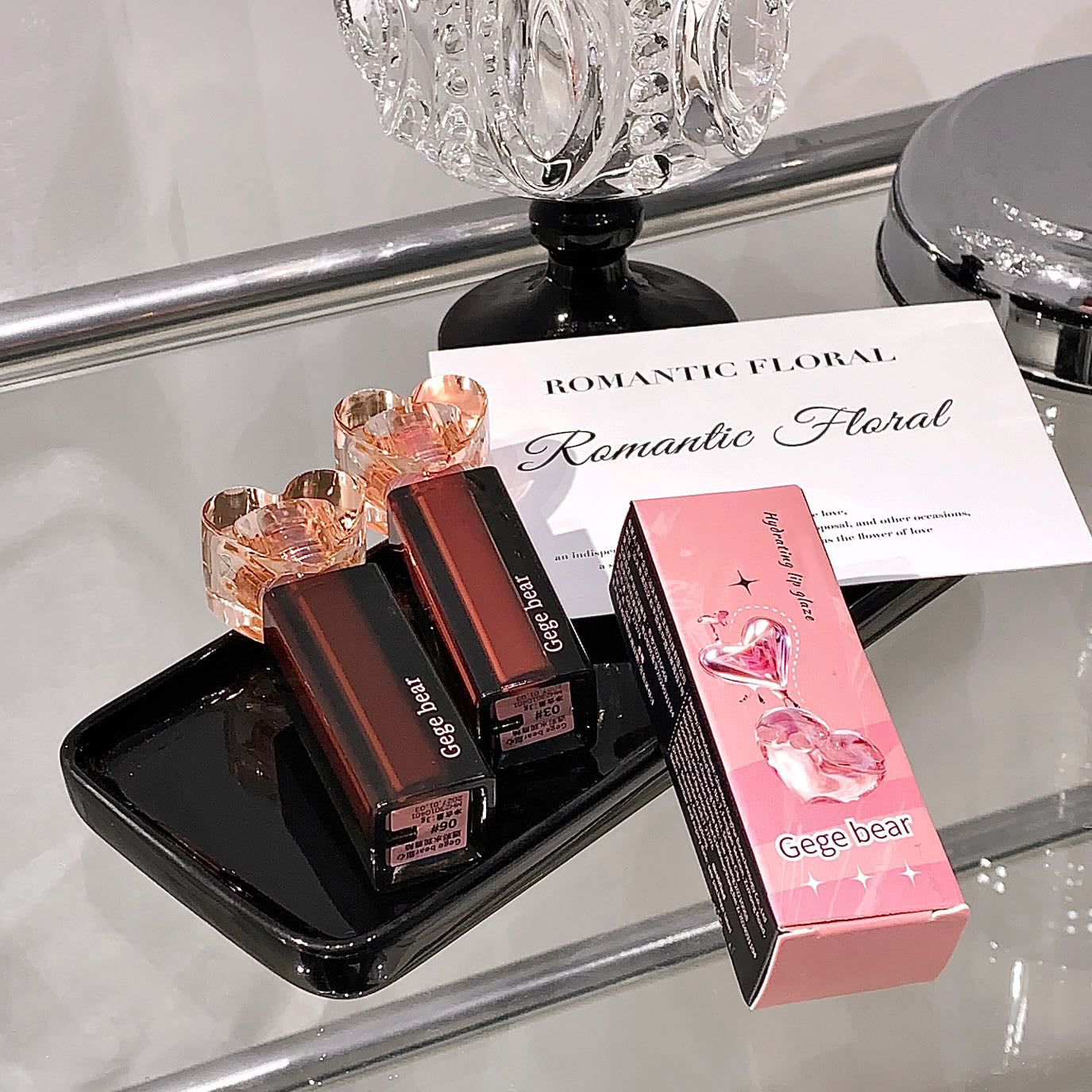 Two lipsticks and a pink box with 'Gege bear' branding on a reflective surface.
