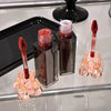 Two lip gloss products with applicators on a reflective surface