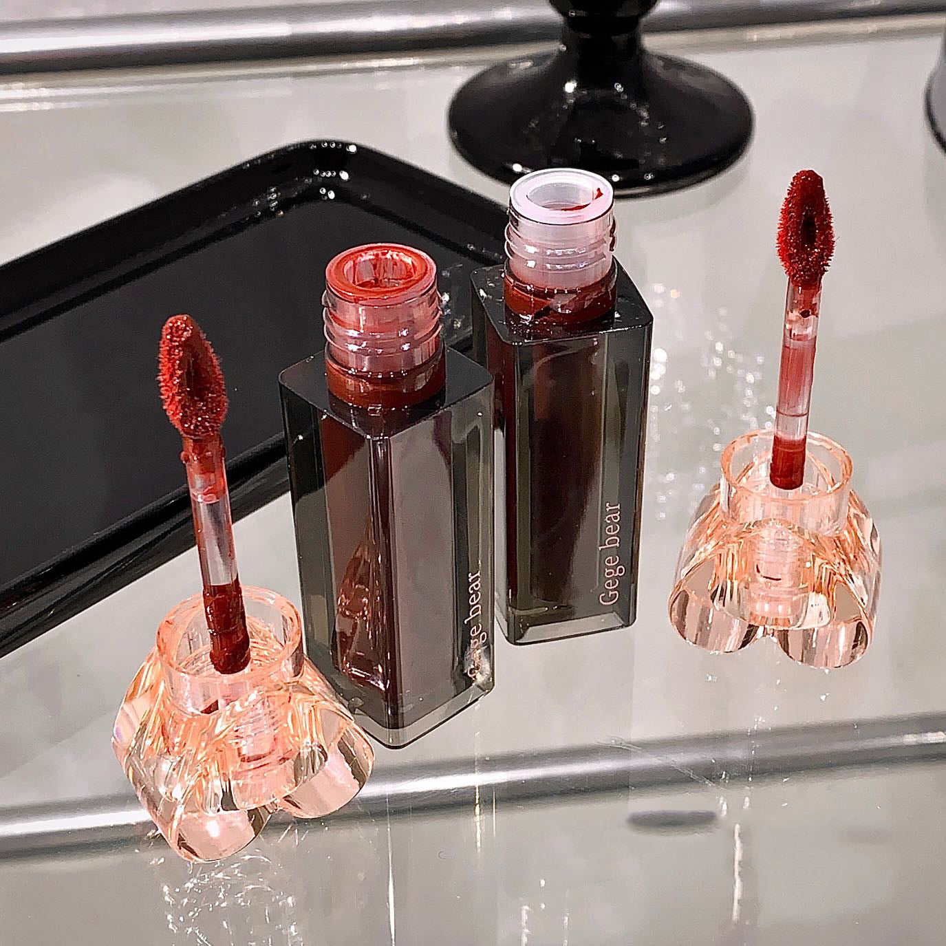 Two lip gloss products with applicators on a reflective surface
