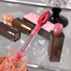 Close-up of a pink lip gloss with applicator on a reflective surface