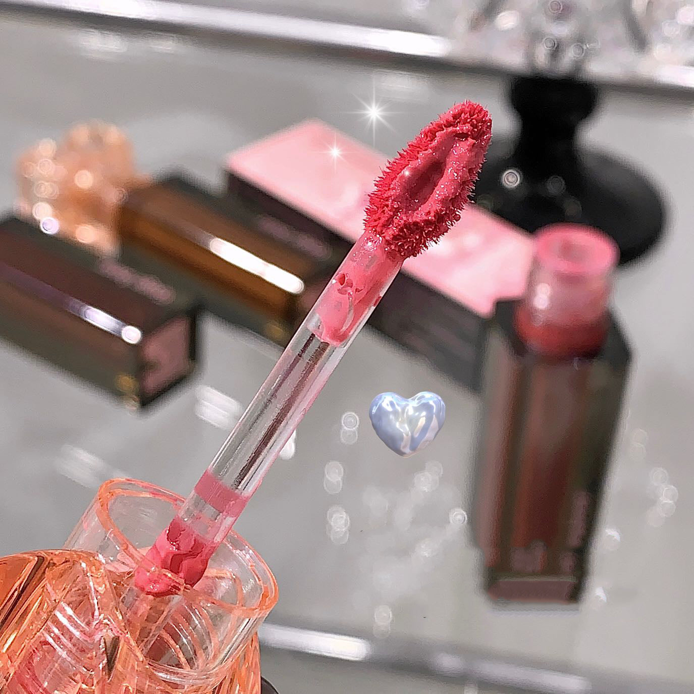 Close-up of a pink lip gloss with applicator on a reflective surface