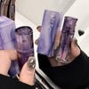 Purple cosmetic products held by a person with a mirror reflection.