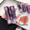 Two purple makeup products held by a hand with a blurred background
