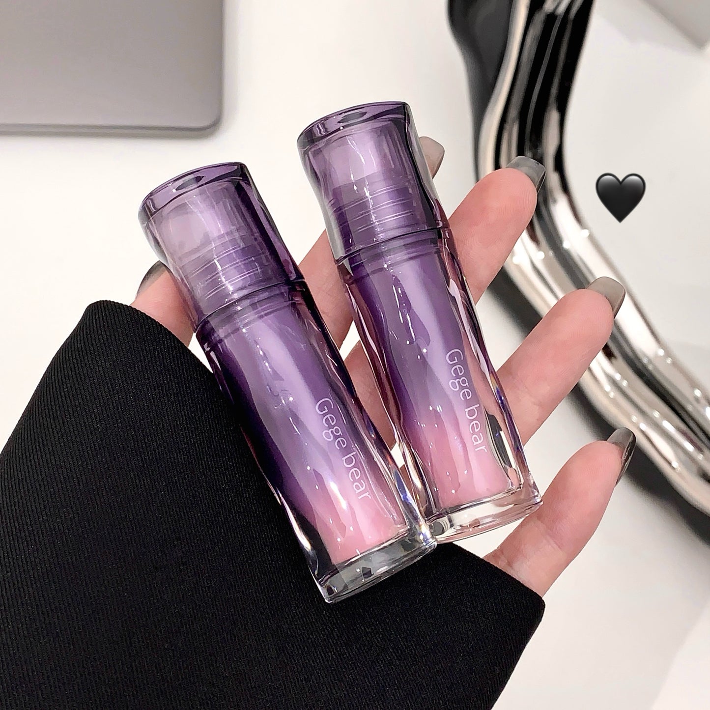 Two purple lip glosses held in a hand with a blurred background