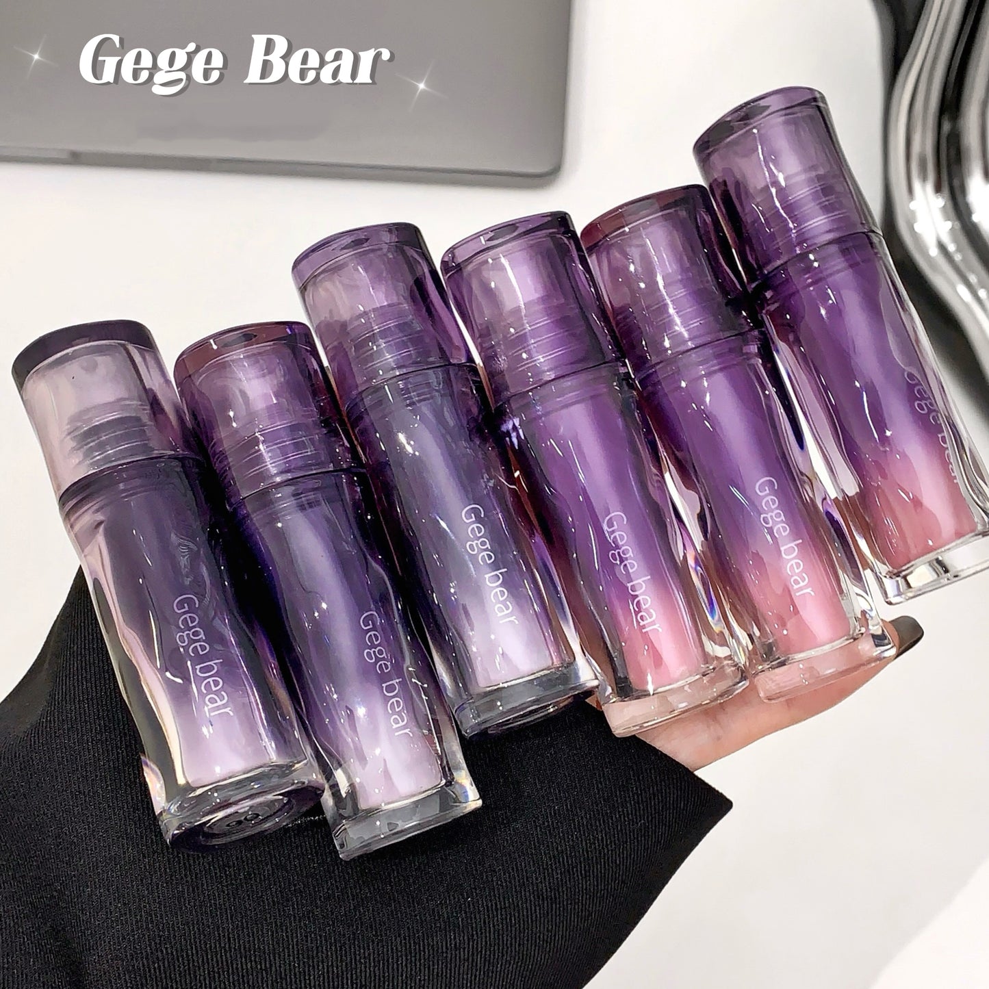 Set of purple lip glosses held by a hand with 'Gege Bear' branding.