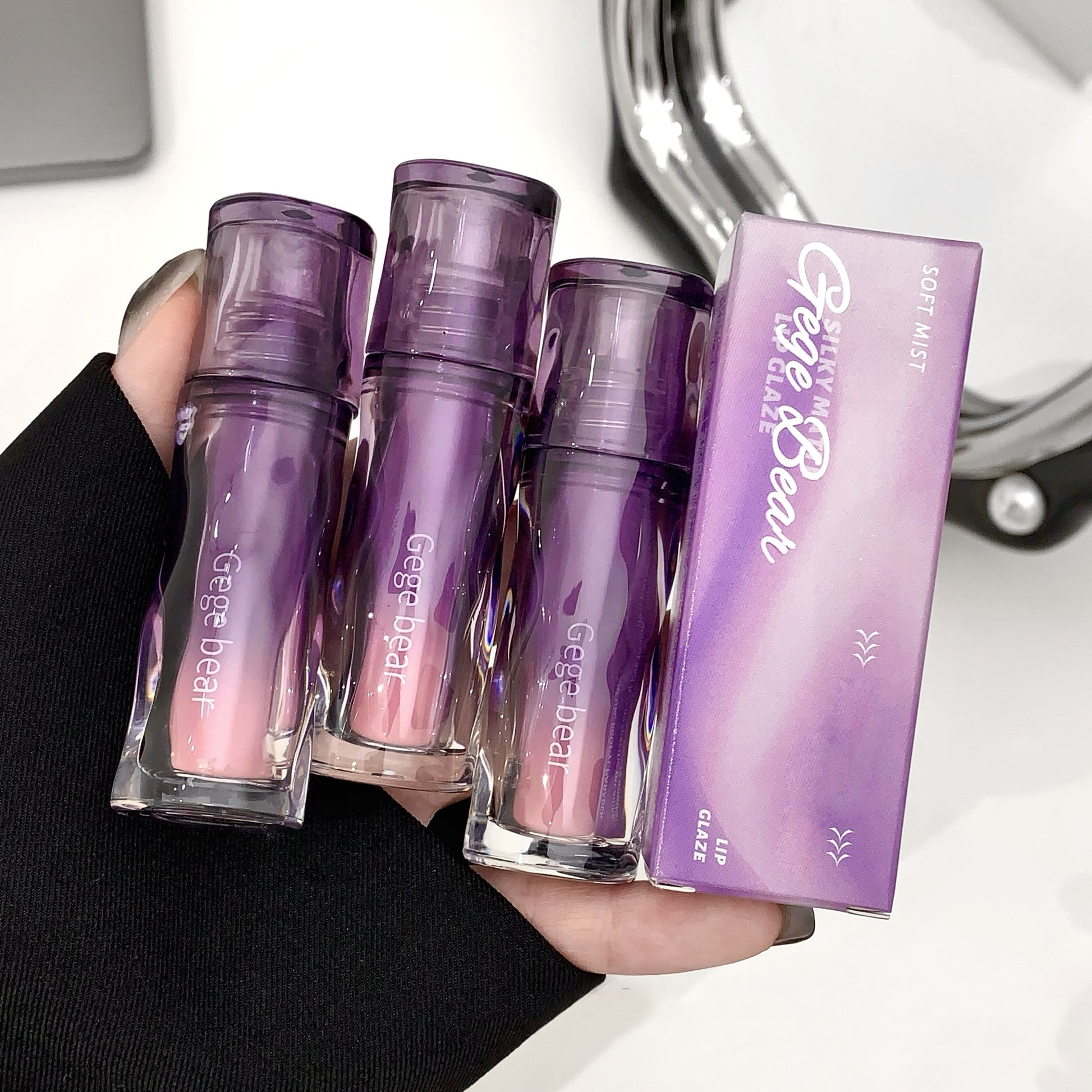 Set of purple makeup products with 'Gene' branding held by a hand against a blurred background.