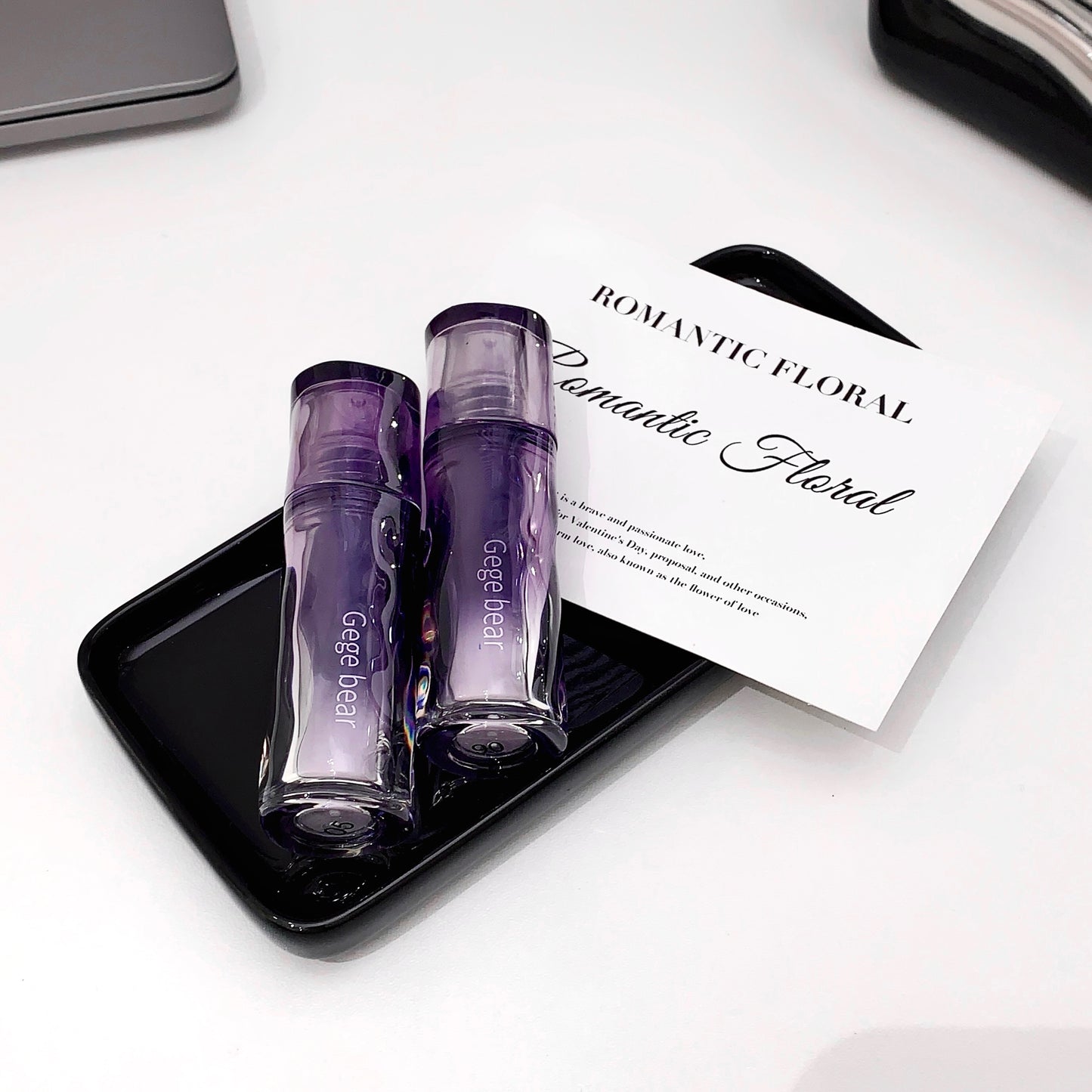 Two purple perfume bottles on a black tray with a 'Romantic Floral' card in the background.