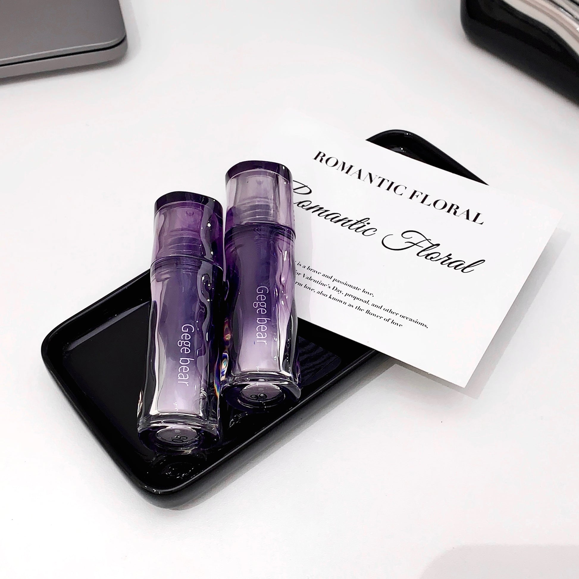 Two purple perfume bottles on a black tray with a 'Romantic Floral' card in the background.