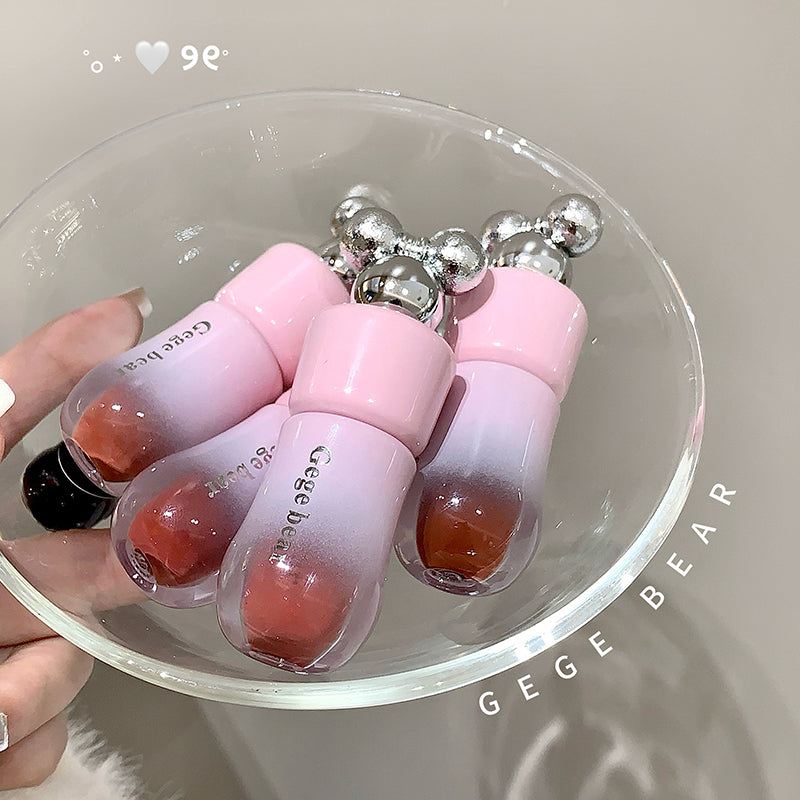 Pink and white lip glosses with a cherry-like texture on a clear dish, branded 'GEGE BEAR'.