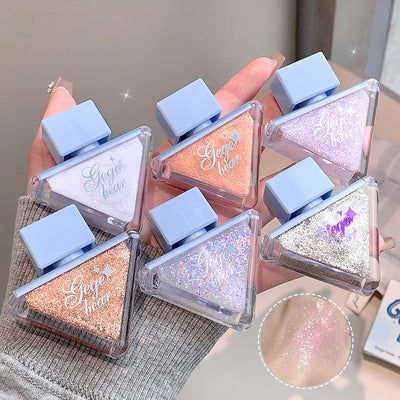 Multiple small cosmetic containers with glittery contents held by a hand, with a close-up of glitter on a gray surface.