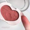 Heart-shaped blush compact with a finger touching the blush, on a light background.