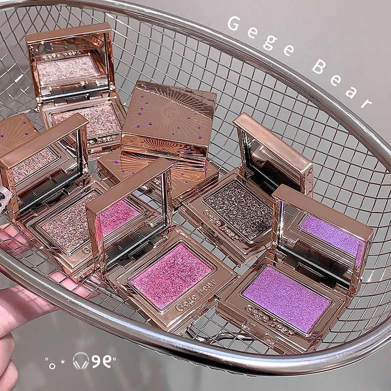 Makeup products with glittery shades on a metal tray, branded 'Gege Bear'.