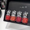 Four small red and silver bottle-shaped charms on a black tray.