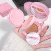 Pink compact powder with a sponge puff held by a hand, with a laptop in the background.