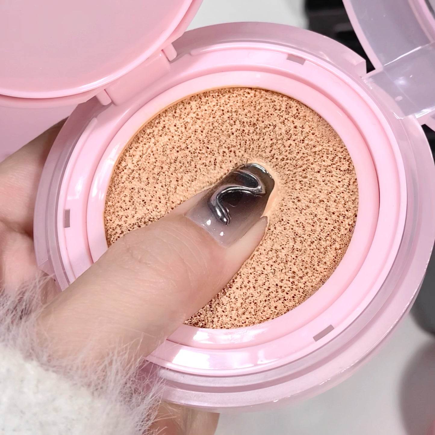 Pink compact powder with a sponge puff inside, held by a hand.