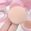 Makeup sponge held by a hand with pink makeup case in the background