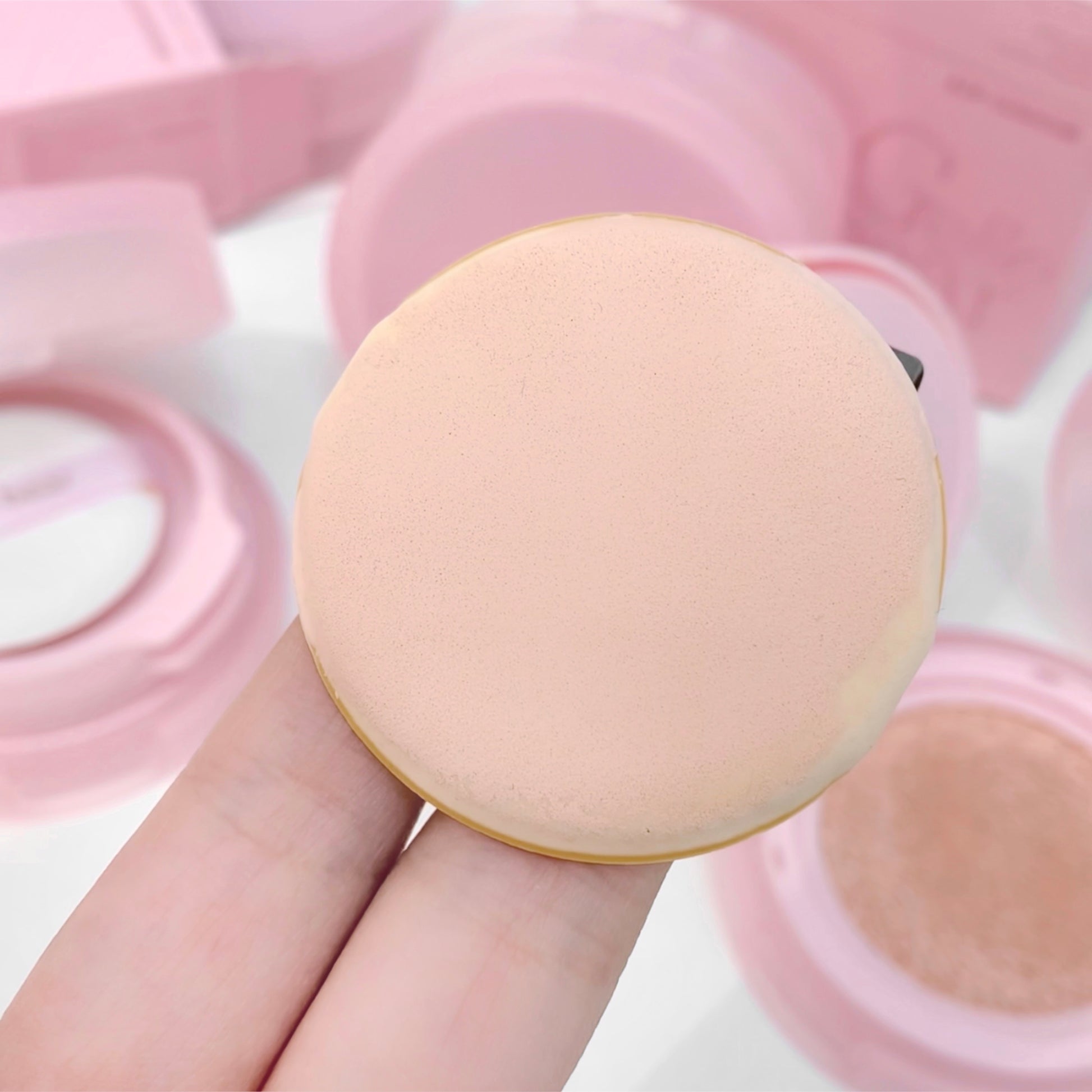 Makeup sponge held by a hand with pink makeup case in the background