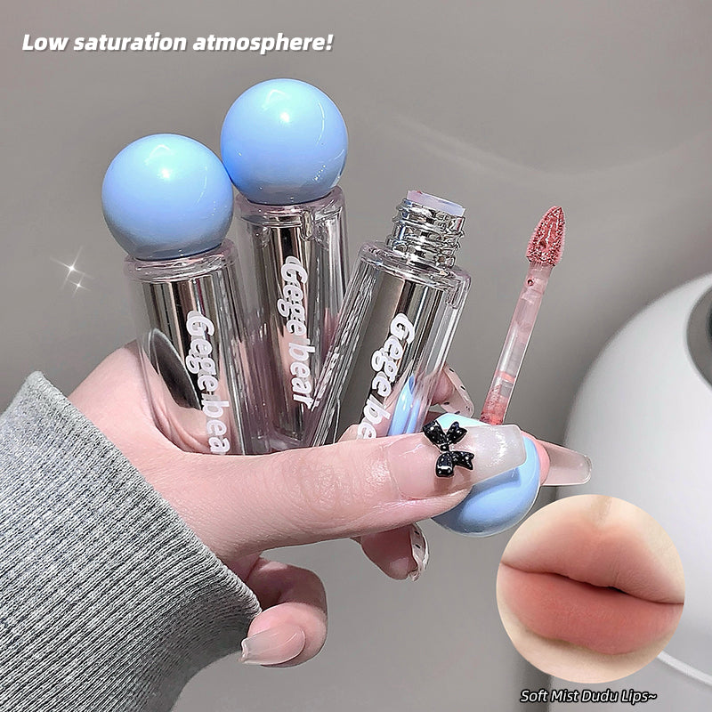 Hand holding two lip glosses with 'Gegenea' branding, one with a brush applicator, on a neutral background.
